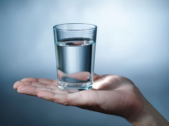 Ein gef&uuml;lltes Wasserglas steht mittig auf einer ausgestreckten Hand vor neutral-blauem Hintergrund. Das Motiv visualisiert Vertrauen, Hygiene und verl&auml;ssliche Trinkwasseranalytik. Ideal zur Darstellung unabh&auml;ngiger Pr&uuml;f- und Laborleistungen f&uuml;r Wasserversorger, Geb&auml;udebetreiber und regulierte Anwendungen.